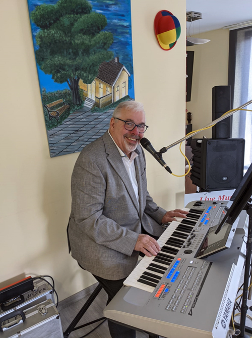 Uli Lau sitzt bei einem Auftritt an seinem Keyboard und lacht.
